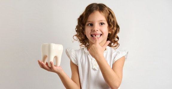 Kind lächelt mit Zahn in der Hand